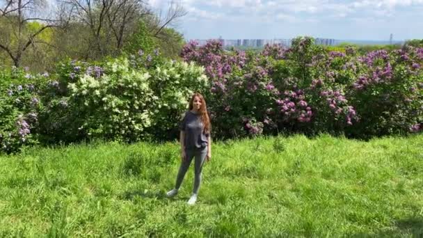 若い女性が咲くライラックの背景にスピンします キエフの街はドニーパーの向こうの背景で見ることができます カメラをオブジェクトから離す 高品質の4K映像 — ストック動画