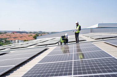 Çatıdaki mühendis güneş panellerinin yanında diz çöküyor. Kurulum için gerekli aletle voltaik fotoğraf çekiliyor.