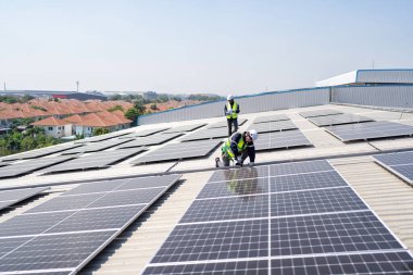 Çatıdaki mühendis güneş panellerinin yanında diz çöküyor. Kurulum için gerekli aletle voltaik fotoğraf çekiliyor.