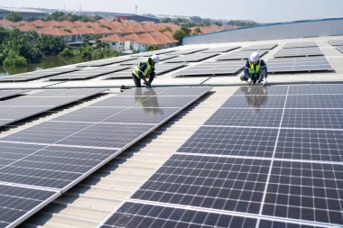 Çatıdaki mühendis güneş panellerinin yanında diz çöküyor. Kurulum için gerekli aletle voltaik fotoğraf çekiliyor.