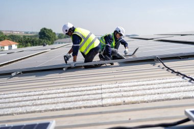 Çatıdaki mühendis güneş panellerinin yanında diz çöküyor. Voltaik kontrol bilgisayarı iyi kurulum için.