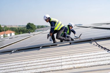 Çatıdaki mühendis güneş panellerinin yanında diz çöküyor. Voltaik kontrol bilgisayarı iyi kurulum için.