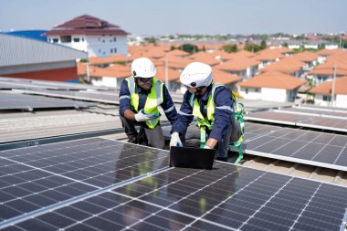 Çatıdaki mühendis güneş panellerinin yanında diz çöküyor. Voltaik kontrol bilgisayarı iyi kurulum için.