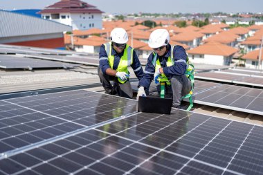 Engineer on rooftop kneeling next to solar panels photo voltaic check laptop for good installation clipart