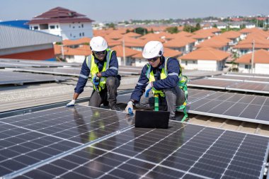 Çatıdaki mühendis güneş panellerinin yanında diz çöküyor. Voltaik kontrol bilgisayarı iyi kurulum için.