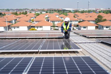 Çatıdaki mühendis güneş panellerinin yanında diz çöküyor. Kurulum için gerekli aletle voltaik fotoğraf çekiliyor.