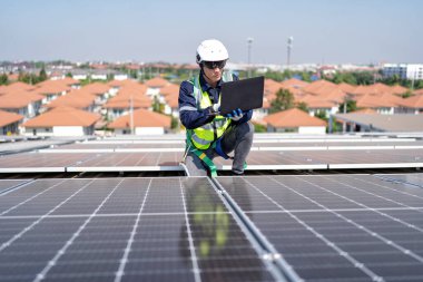 Çatıdaki mühendis güneş panellerinin yanında diz çöküyor. Voltaik kontrol bilgisayarı iyi kurulum için.