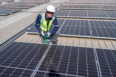 Çatıdaki mühendis güneş panellerinin yanında diz çöküyor. Kurulum için gerekli aletle voltaik fotoğraf çekiliyor.