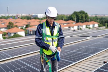 Çatı katında güneş panellerinin yanında duran mühendis güvenlik önlüğü giyer, eldiven giyer ve çalışmaya hazırdır.