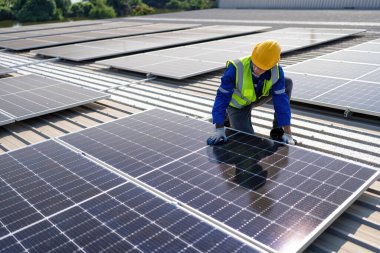 Çatıdaki mühendis güneş panellerinin yanında diz çöküyor. Kurulum için gerekli aletle voltaik fotoğraf çekiliyor.