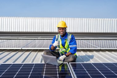 Çatıda güneş panellerinin yanında oturan mühendis kurulum için fotoğraf voltaik kontrol dizüstü bilgisayarı