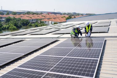 Çatıdaki mühendis güneş panellerinin yanında diz çöküyor. Kurulum için gerekli aletle voltaik fotoğraf çekiliyor.