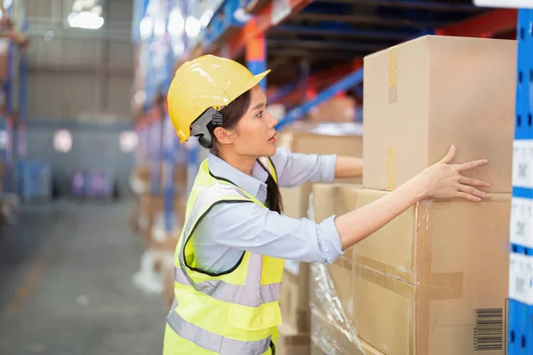 Staff working in large depot storage warehouse lift up heavy carton box to shelf