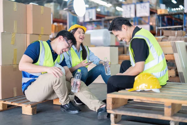 Staff in large storage warehouse together sit back relax funny laughing check mobile phone