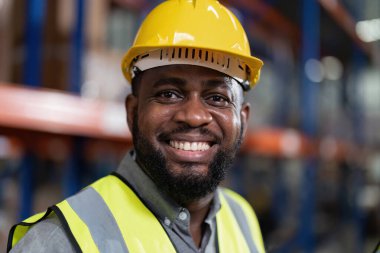 Depoda çalışan Afrikalı Amerikalı forkliftleri kontrol ediyor, gülümsüyor.