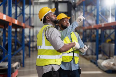 Depoda çalışan Afrikalı Amerikalılar, forklift kamyonlarını kontrol ediyorlar, kutuları yüklüyorlar, gülümsüyorlar ve ellerini kontrol ediyorlar.