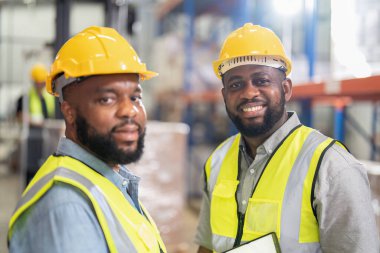 Depoda çalışan Afrikalı Amerikalılar, forklift kamyonlarını kontrol ediyorlar, kutuları yüklüyorlar, gülümsüyorlar. 