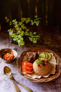 Tahta tabakta kebuli pilavı ızgara et, domates ve salatalık ile servis edilir.