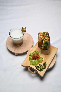 glass of honey starfruit ginger shake on a wooden plate and a plate of keumamah eat toast on a white cloth.