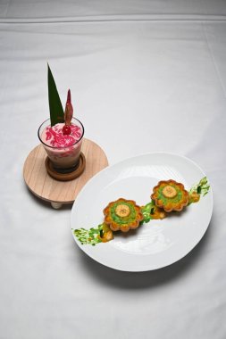 glass of sanger cendol bungong kala on a wooden plate and a plate of pie peungat on a white cloth.