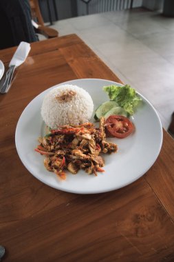 nasi ayam kecombrang, a serving of kecombrang chicken rice on a wooden table. natural light.