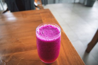 a glass of dragon fruit juice on a wooden table. natural light. jus buah naga.