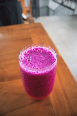 a glass of dragon fruit juice on a wooden table. natural light. jus buah naga.