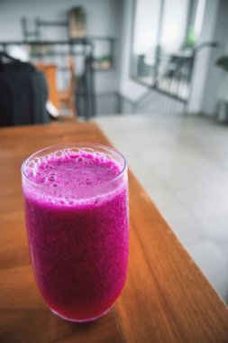 a glass of dragon fruit juice on a wooden table. natural light. jus buah naga.