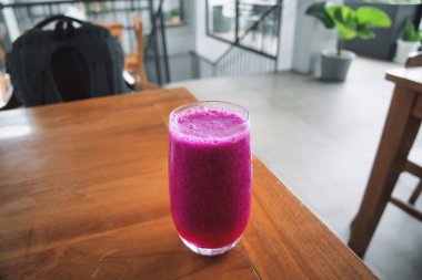 a glass of dragon fruit juice on a wooden table. natural light. jus buah naga.