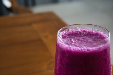 a glass of dragon fruit juice on a wooden table. natural light. jus buah naga.