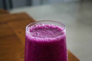 a glass of dragon fruit juice on a wooden table. natural light. jus buah naga.