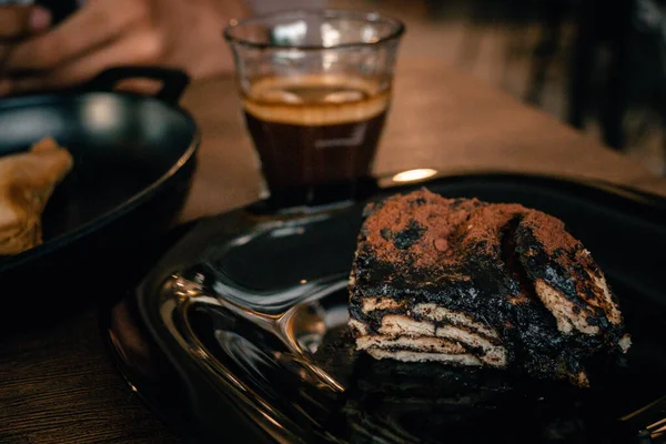 a piece of cake and a glass of coffee on a wooden table for breakfast.