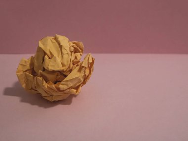 Ball of crumpled peach-colored paper on a pink pastel background. Minimal concept, flat lay.