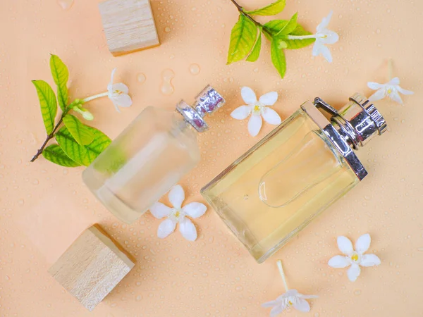 Two bottles of perfume on a peach background, fresh white floral decoration wooden cubes.