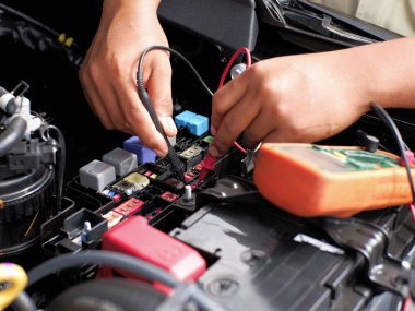 Araba tamircisi sigorta kutusunda bir çoklu metre ve bir test kalemi kullanarak sigorta bağlantısını kontrol ediyor