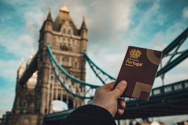 London, UK - 2023: Hand holding a portuguese passport in front of the Tower Bridge. clipart