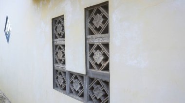 Betondan yapılmış geometrik desenli havalandırmalı duvarlar inşa ediyorlar. Duvarların eskimiş duvar dokusuyla sarımsı rengi klasik ve klasik bir izlenim veriyor..