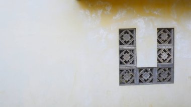 Betondan yapılmış geometrik desenli havalandırmalı duvarlar inşa ediyorlar. Duvarların eskimiş duvar dokusuyla sarımsı rengi klasik ve klasik bir izlenim veriyor..