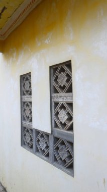 Betondan yapılmış geometrik desenli havalandırmalı duvarlar inşa ediyorlar. Duvarların eskimiş duvar dokusuyla sarımsı rengi klasik ve klasik bir izlenim veriyor..