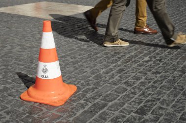 Barselona şehrinin armalı trafik konisi ve yakınlarda yürüyen insanlar. Bu nesne İspanya 'nın Barselona kentindeki Sant Jaume Meydanı' nda bulundu..