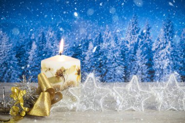 Mumlu Noel süslemesi, altın yay, gümüş yıldızlar, mavi bir orman arka planında.