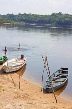 Brezilya 'da Amazon Nehri kıyısına demirlemiş eski ahşap kayıklar ve içinde yüzen iki adam..
