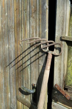 An old spading fork positioned against an old door left ajar, casts a creepy shadow on it clipart