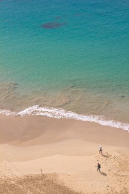 Güneşli bir günde Fernando de Noronha, Brezilya 'da turkuaz bir suyla renkli bir sahil kıyısında yürüyen insanların görüntüsü.