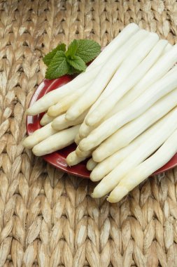 Arka planda hasır masa olan bir tabağa beyaz kuşkonmaz konmuş.