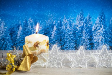 Mumlu Noel süslemesi, altın yay, gümüş yıldızlar, mavi bir orman arka planında.