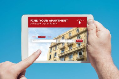 Elinde tablet cihazı olan bir adam bir daire ve kiralık ev sitesine girip arka planda mavi gökyüzü olan bir parmakla ekrana dokunuyor..