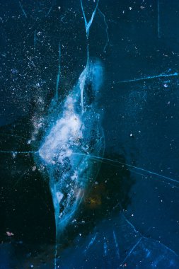 blue ice on the lake or pond with a white impact mark and cracks radiating from it in the winter in the frost during the day