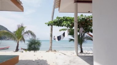 Güzel bir adadaki bir bungalovla palmiye ağacı arasında çamaşır ipinde asılı duran mavi bir okyanus ve arkasında muhteşem kumlu bir plaj olan Koh Phangan, Tayland.