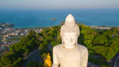 Güneş doğarken Phuket 'in tepesindeki ünlü Büyük Buda heykelinin nefes kesen bir zaman atlaması. Arka planda büyüleyici okyanus ve sahil şeridi var..